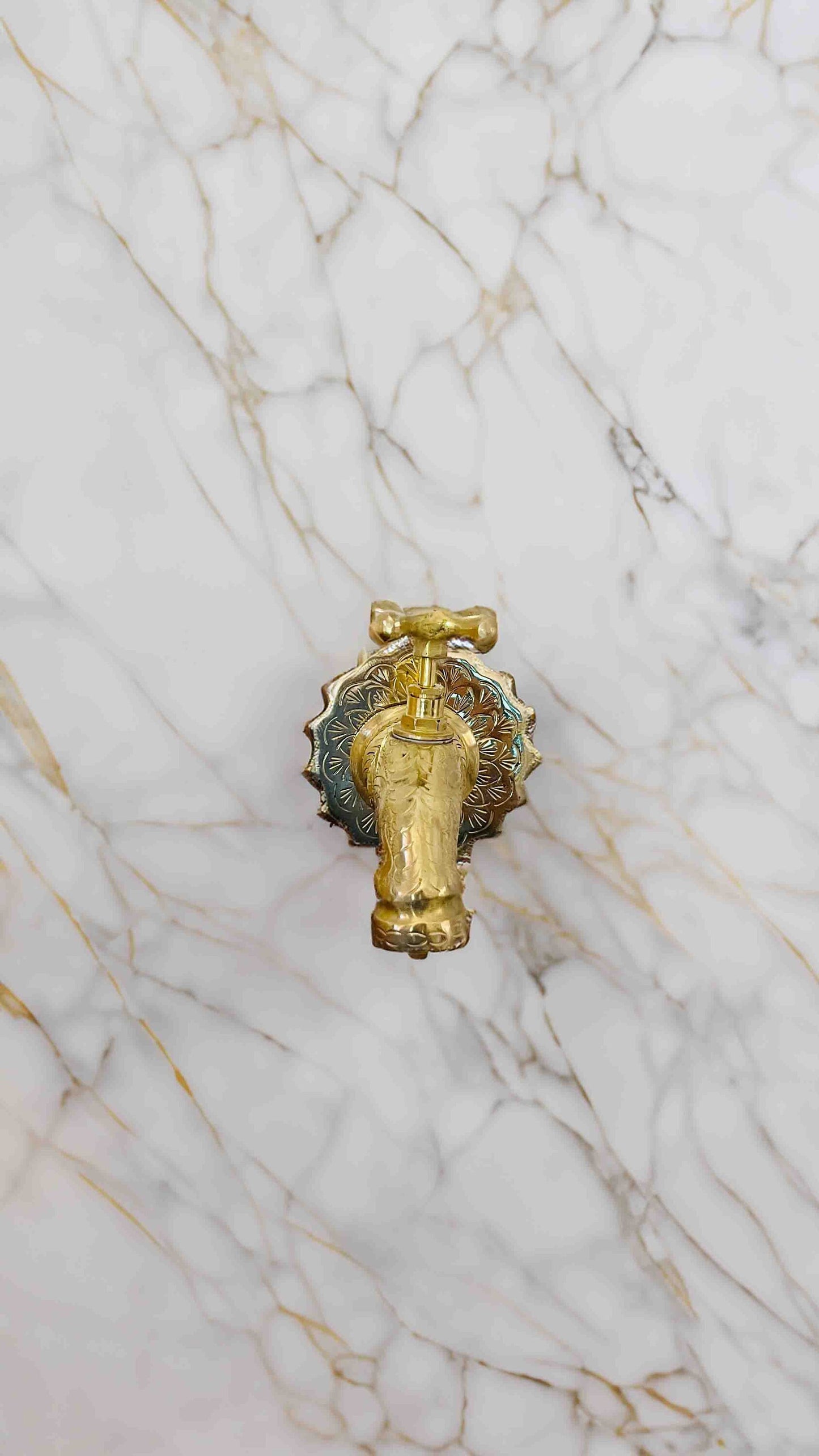 a bathroom sink with a gold faucet and a marble wall