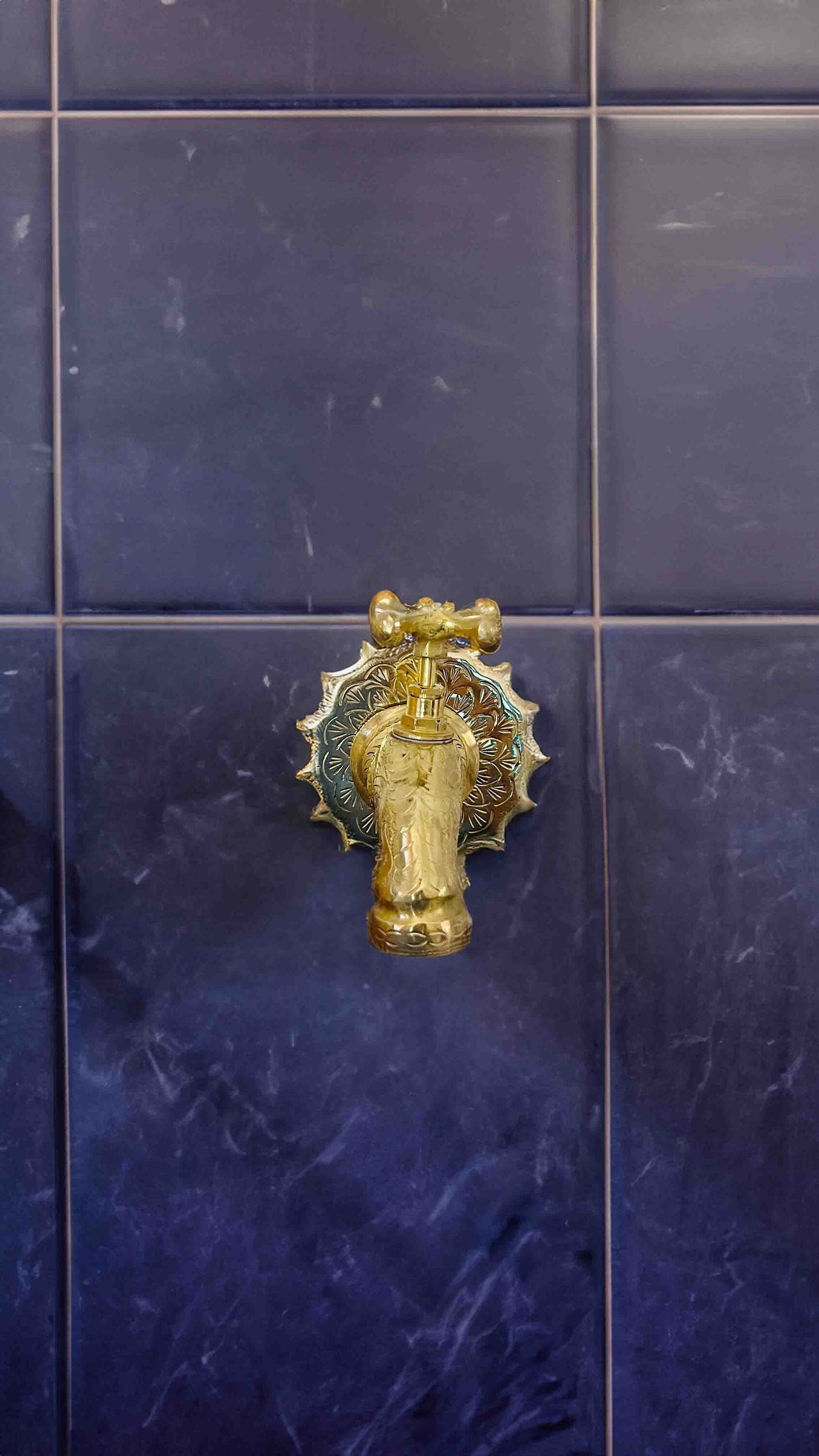 a blue tiled wall with a gold and silver faucet