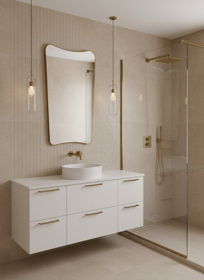 Brass mirror above white vanity in a contemporary beige bathroom with glass shower