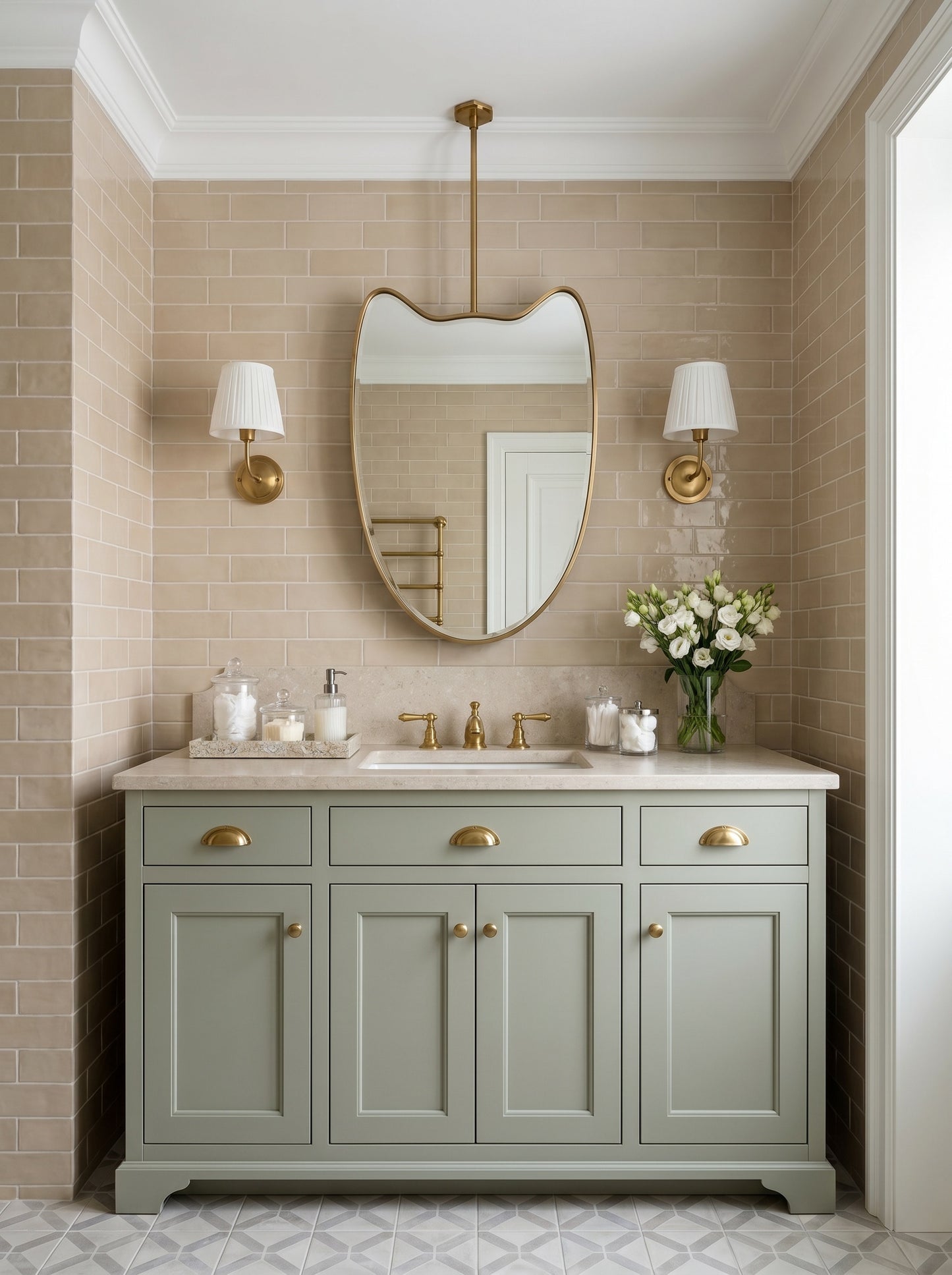 Suspended brass mirror with organic silhouette above a sage green vanity and beige subway tile bathroom.