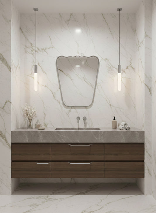 Silver asymmetrical brass mirror above wood vanity in marble bathroom.