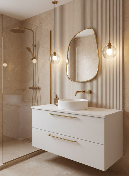 Irregular brass mirror above floating white vanity in a beige marble bathroom.