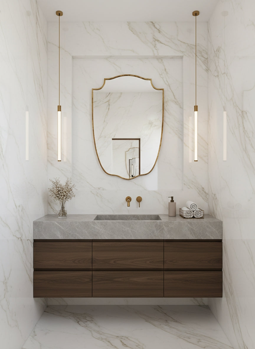 Brass shield mirror in marble bathroom with wood vanity.