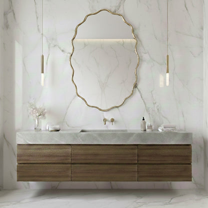 Oval wavy brass mirror above wooden floating vanity in marble bathroom.