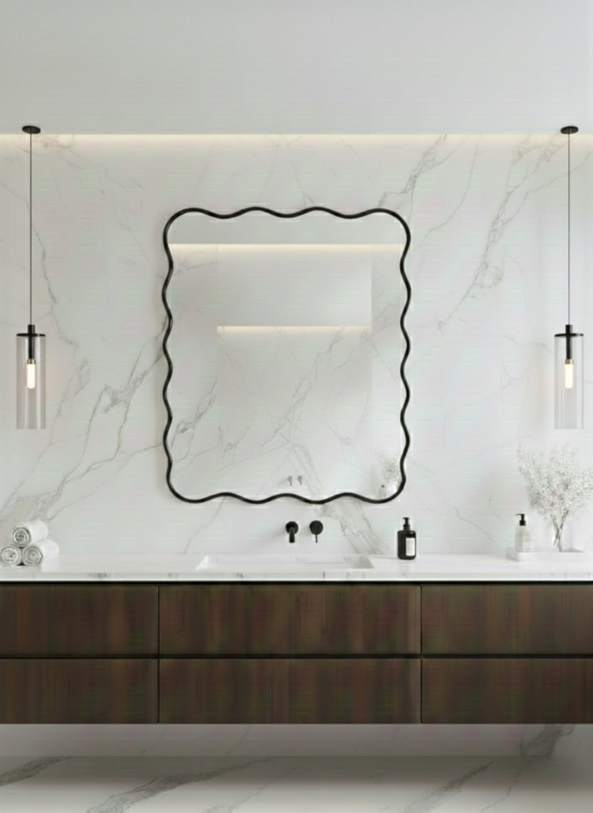 Wavy black brass mirror above modern marble bathroom vanity.