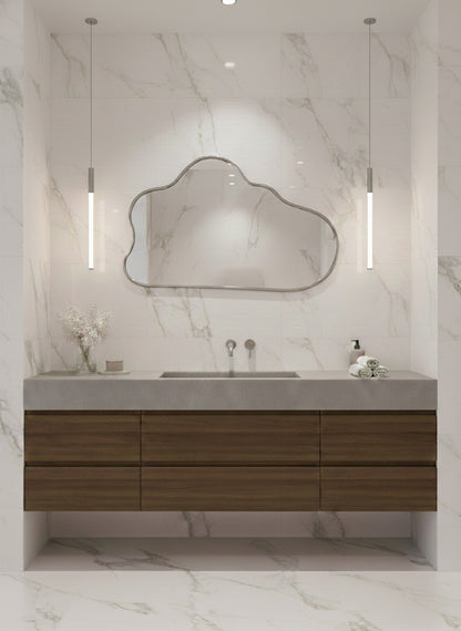 Silver brass cloud mirror above wood floating vanity in marble bathroom.
