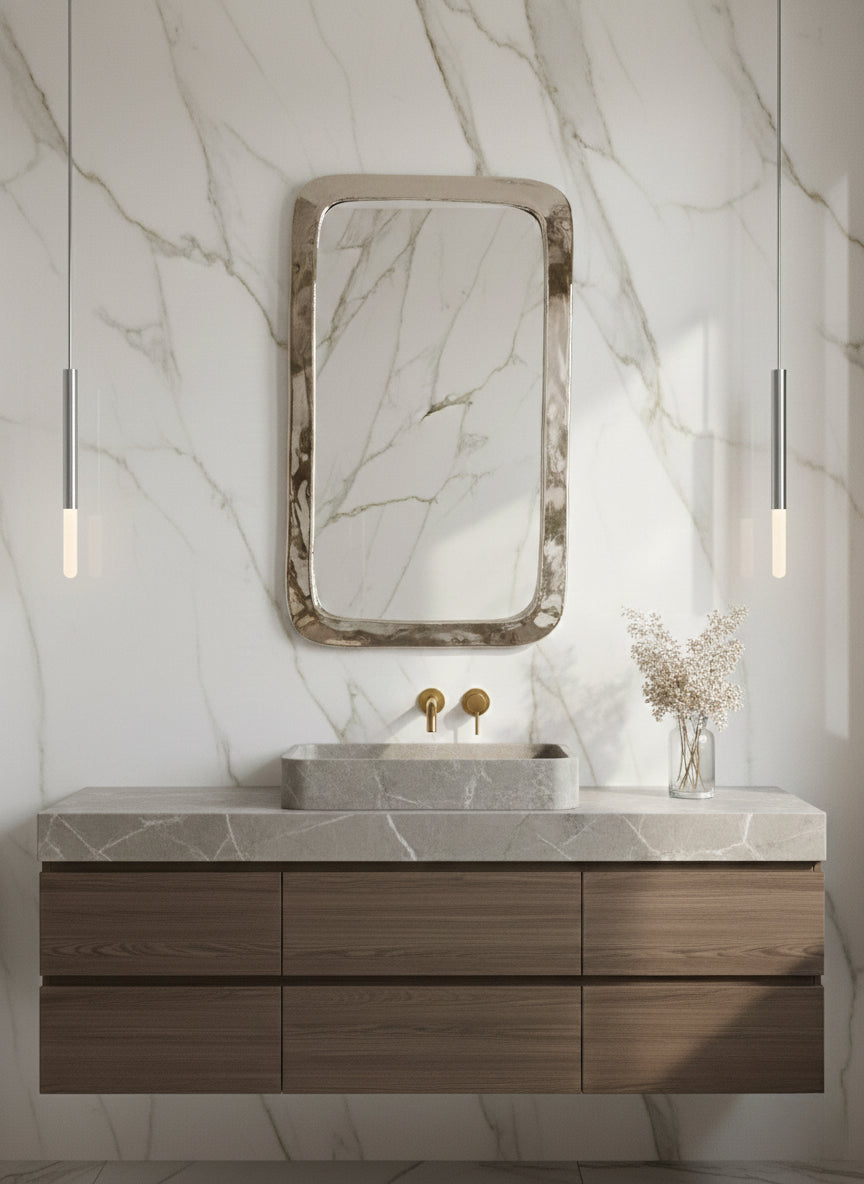 Polished silver rounded rectangle mirror over marble bathroom vanity.