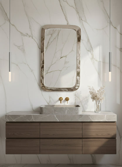 Polished silver rounded rectangle mirror over marble bathroom vanity.