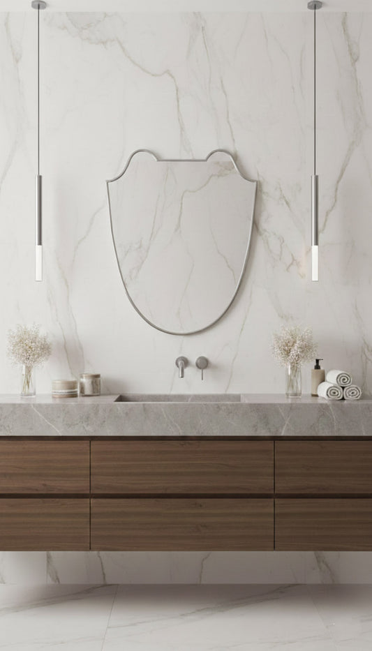 Silver shield brass mirror above wood vanity with marble wall and pendant lights.