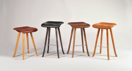 Four stools with different wood finishes on a white background