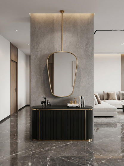 Hanging brass mirror above black console in modern hallway.
