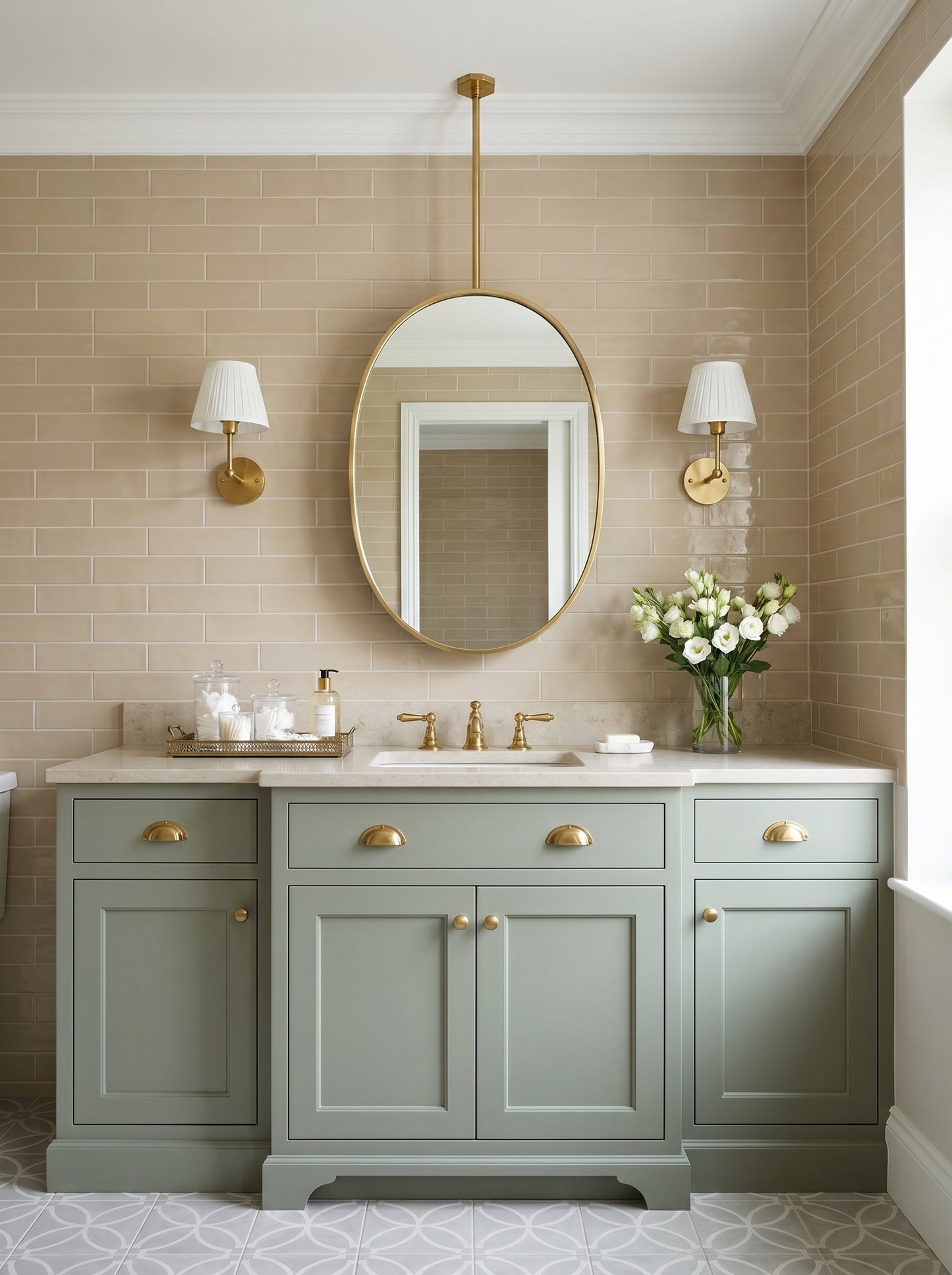 Suspended oval brass mirror above a sage green vanity with brass sconces and beige subway tile bathroom walls.