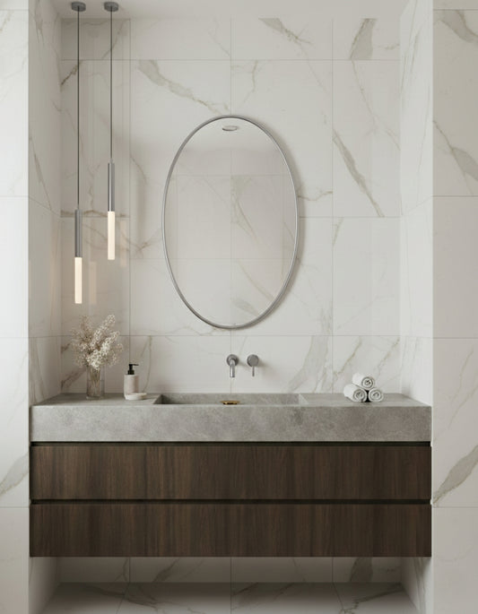 Silver oval mirror above floating wood vanity in modern marble bathroom.
