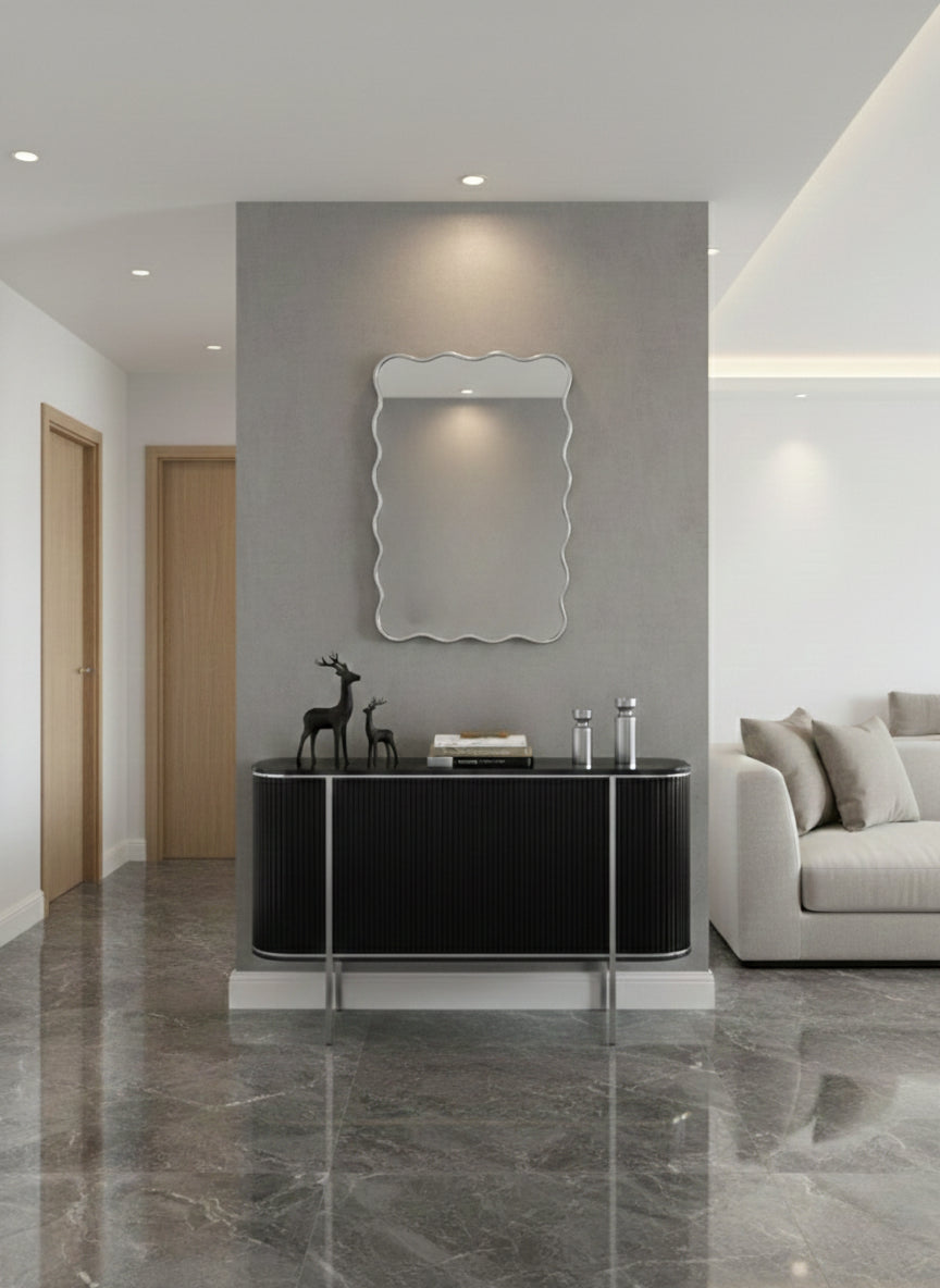 Wavy silver brass wall mirror above black console table.