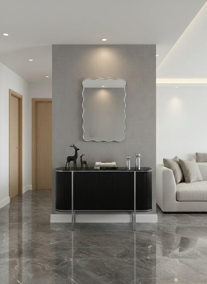 Wavy silver brass wall mirror above black console table.