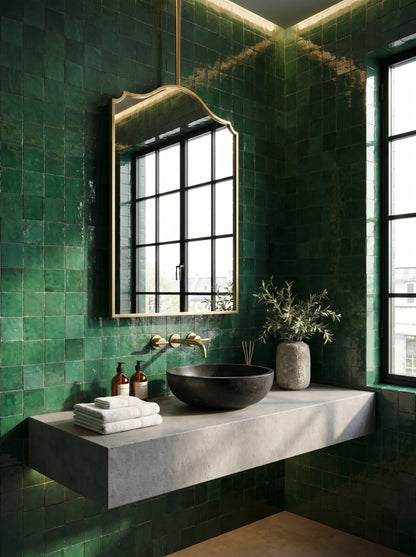Hanging brass arch mirror in a luxury bathroom with emerald green zellige tiles and a black vessel sink.