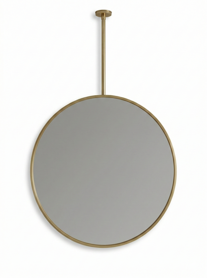 Round brass suspended mirror with ceiling mount on white wall.