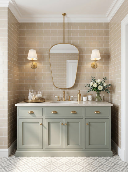 Suspended organic brass mirror above a sage green vanity with brass sconces and beige subway tile bathroom walls.
