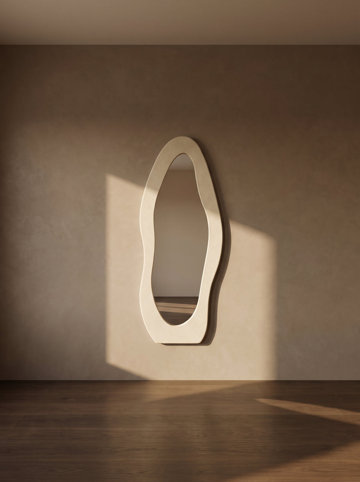 An organic-shaped cream wall mirror with a thick, wavy frame, mounted on a textured beige wall in a room with warm sunlight and a dark wood floor.
