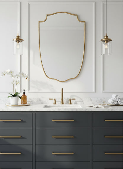 Brass shield mirror above dark blue bathroom vanity.