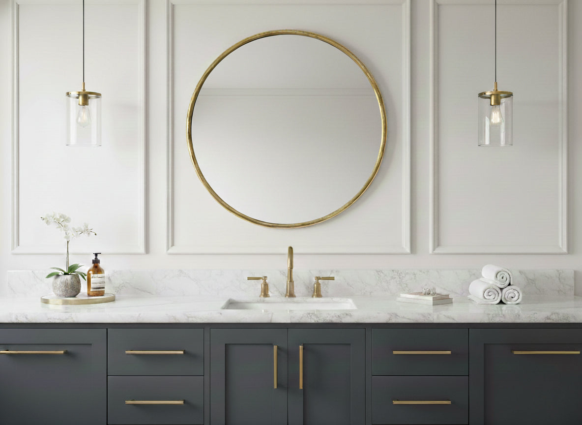 Round brass mirror over a gray floating vanity on a marble bathroom wall.