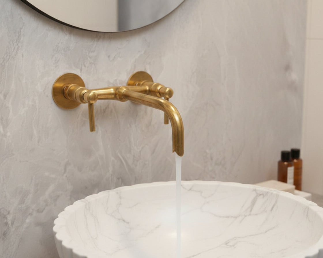 Antique brass wall faucet running over round marble vessel sink.