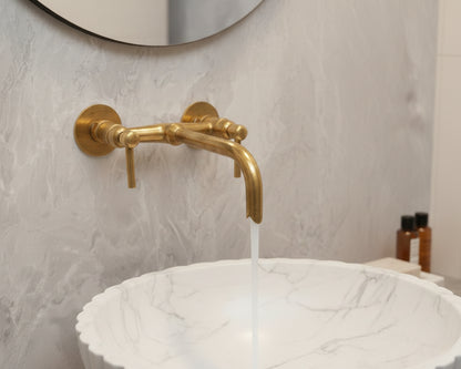 Antique brass wall faucet running over round marble vessel sink.