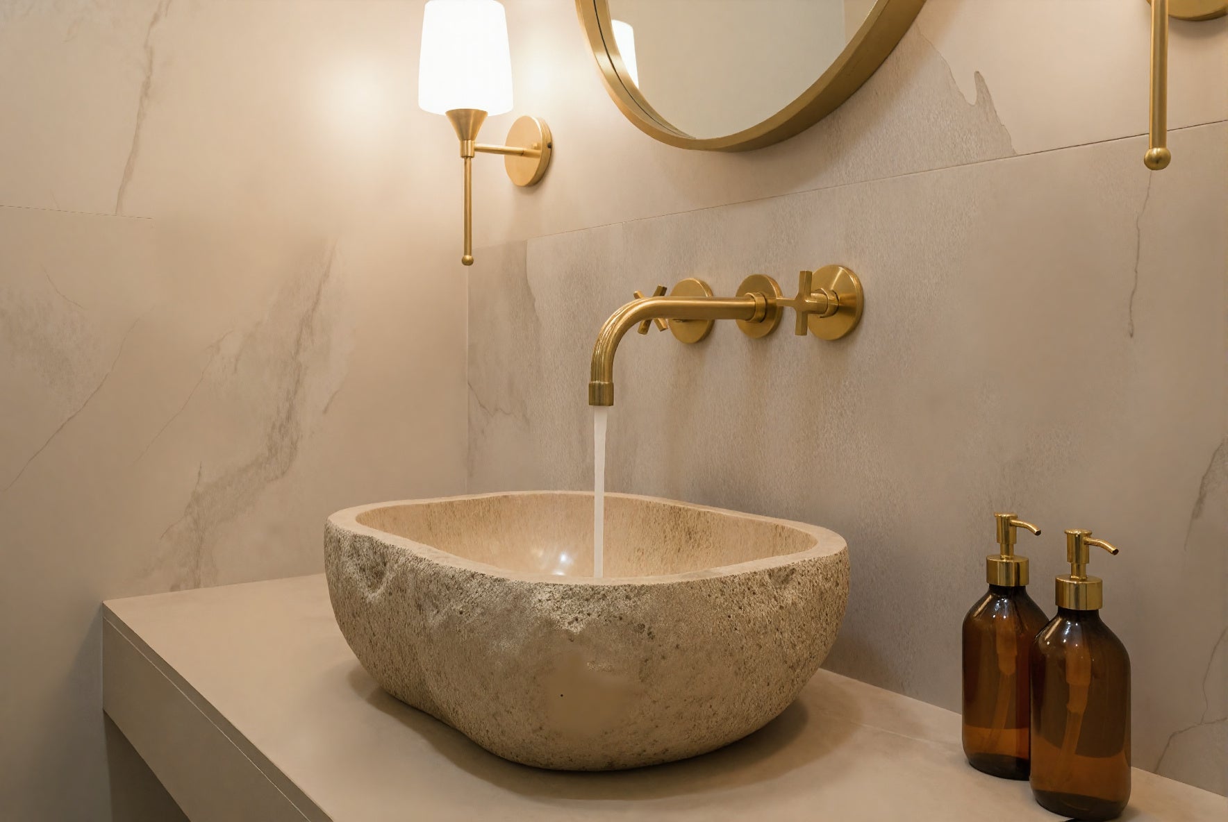 Natural stone vessel sink with wall-mounted brass faucet and marble wall.