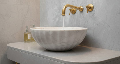 White marble vessel sink with brushed brass wall faucet