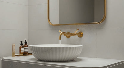Wall-mounted brass faucet over marble vessel sink with brass mirror.