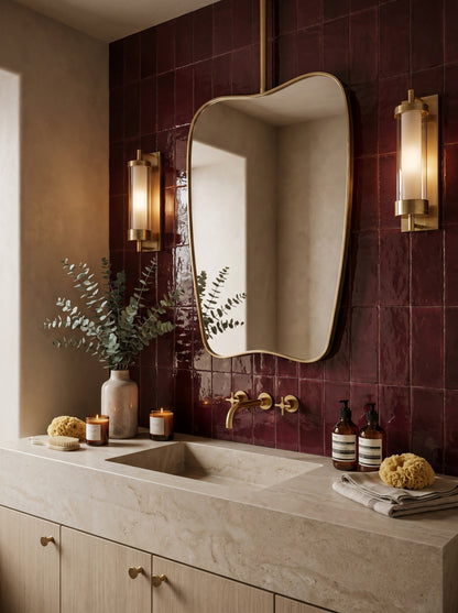 Hanging organic brass mirror in a luxury bathroom with burgundy zellige tiles, stone vanity, and brass sconces.