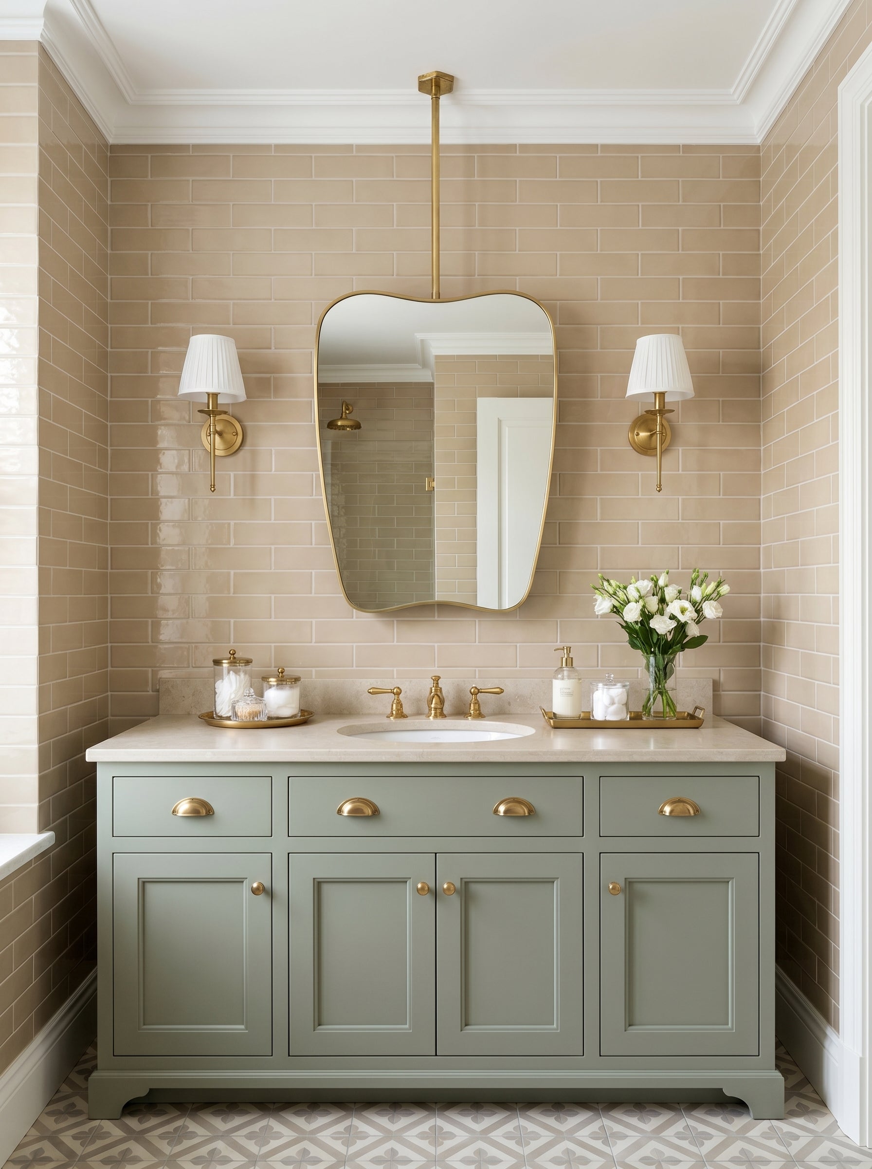 Suspended wavy brass mirror above a sage green vanity with beige subway tiles and brass wall sconces in a traditional bathroom.