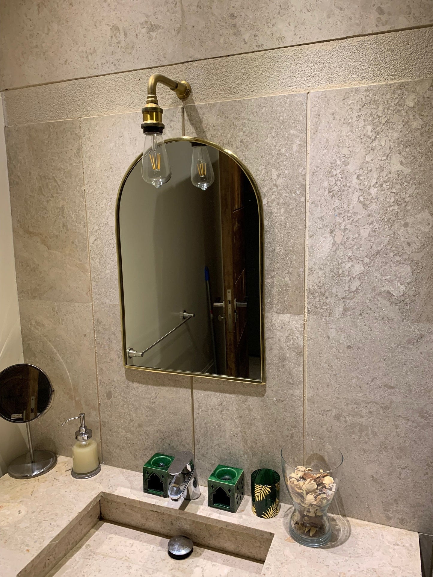 a bathroom with a sink, brass mirror and soap dispenser