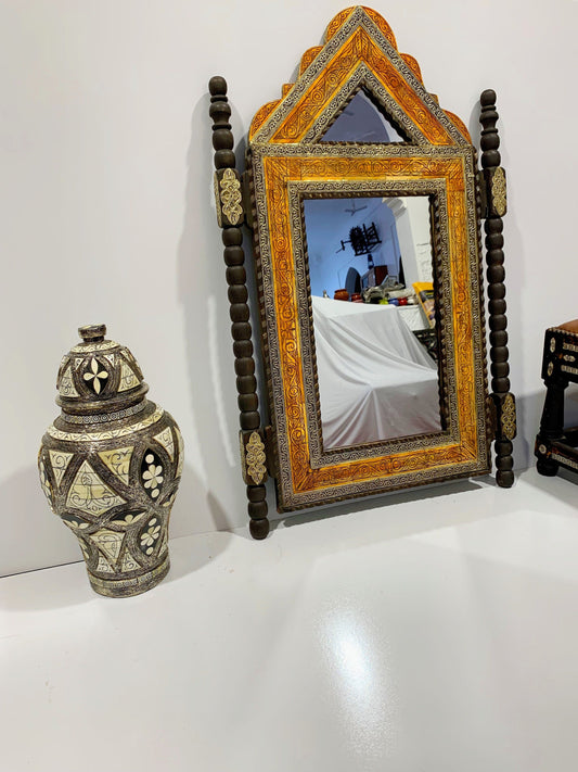 a mirror sitting on top of a table next to a vase