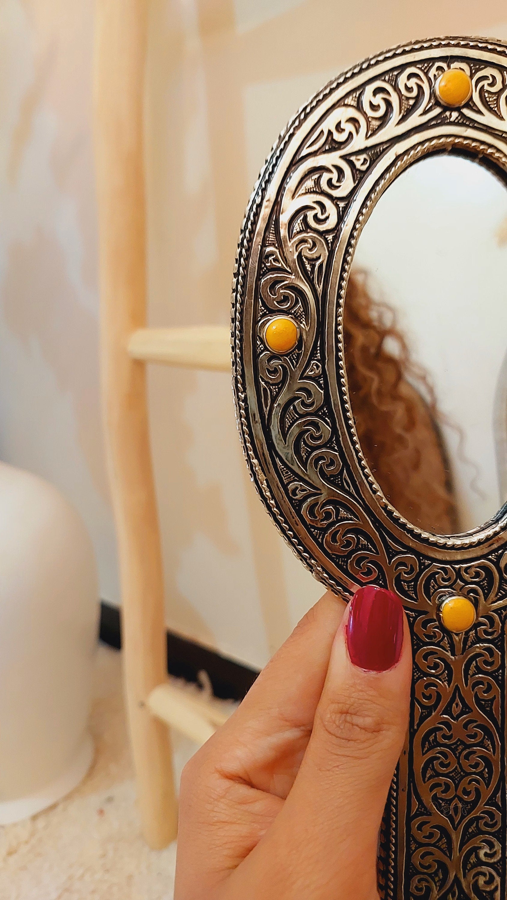 a woman's hand holding up a mirror with yellow beads