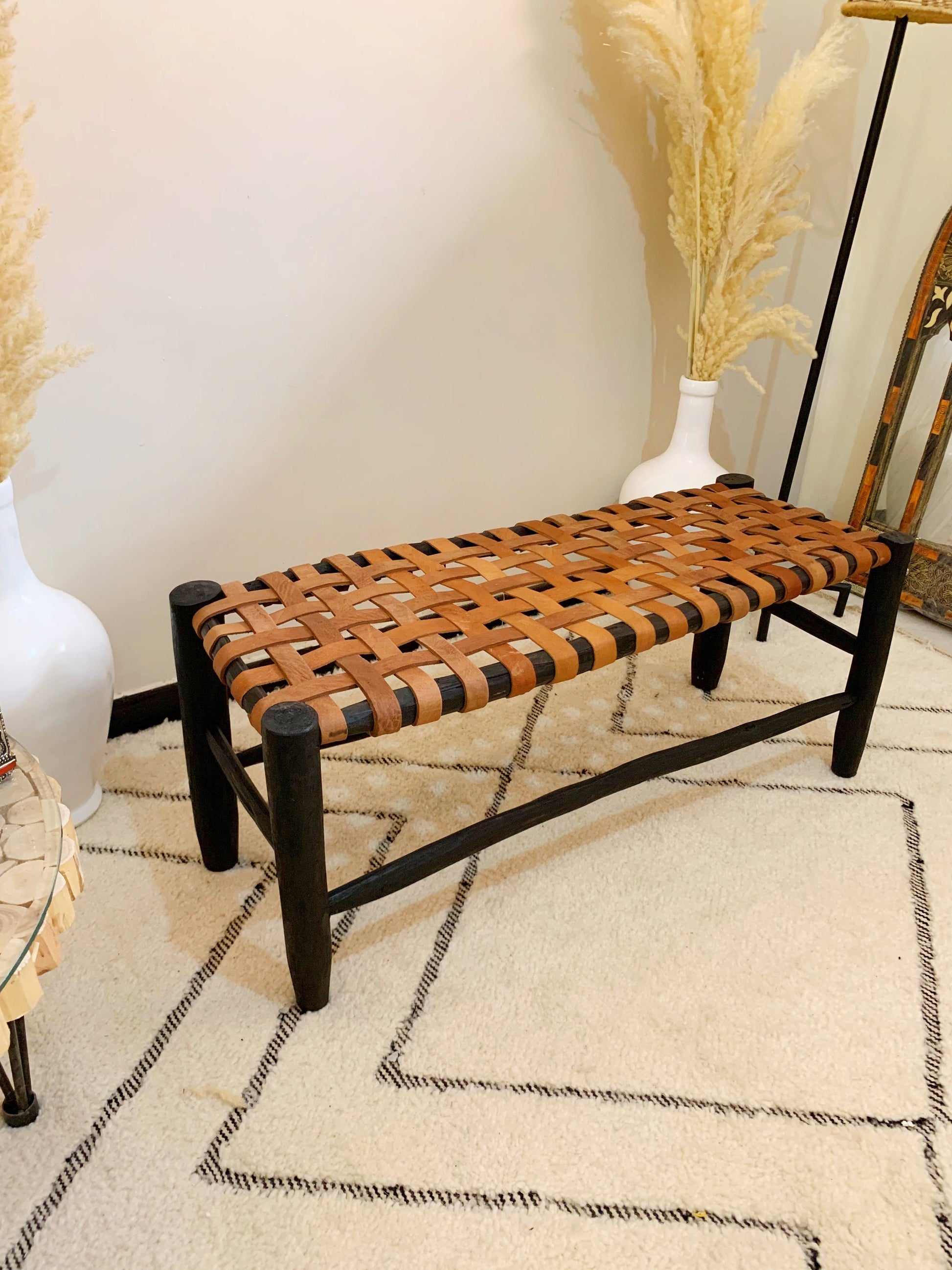 a wooden bench sitting on top of a rug next to a vase