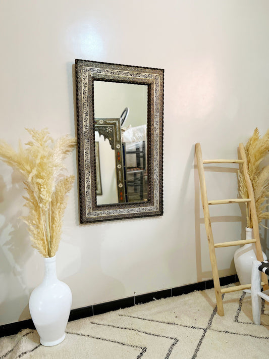 a white vase with a plant in it next to a mirror