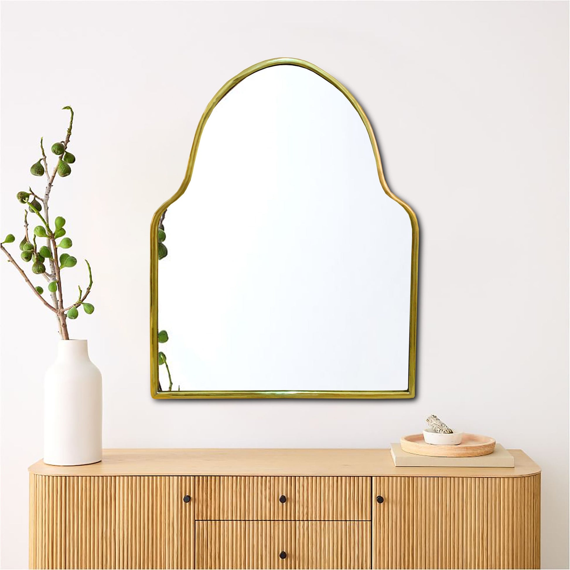 a brass mirror on a wall above a dresser