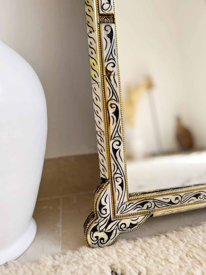 a white vase sitting next to a gold framed mirror