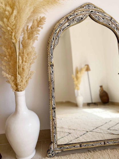 a white vase with a dried plant in it next to a mirror