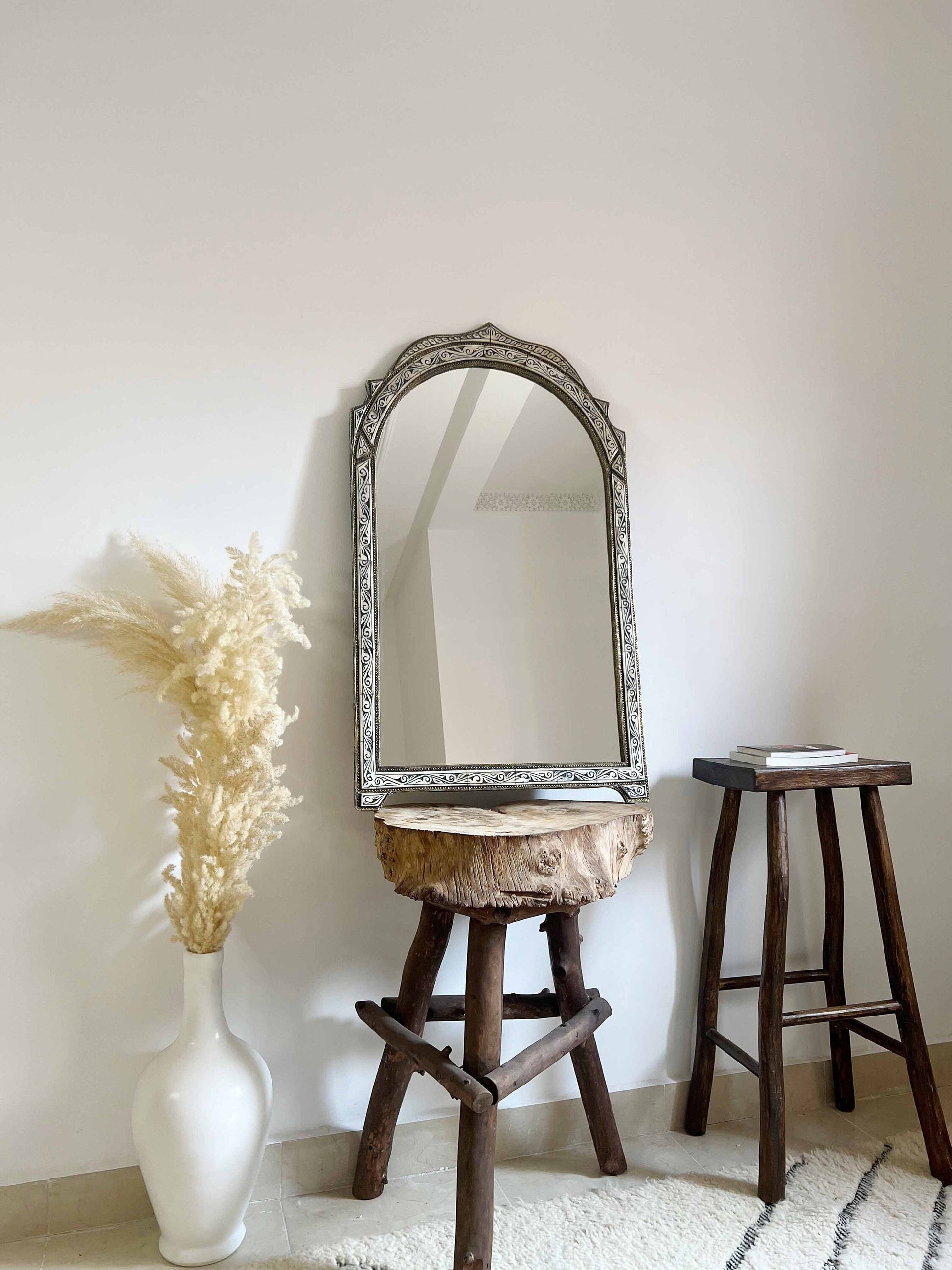 a mirror sitting on top of a wooden stool next to a vase