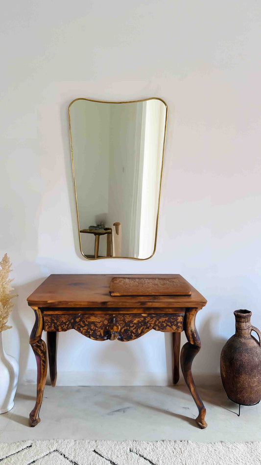 a wooden table with a brass mirror on the wall